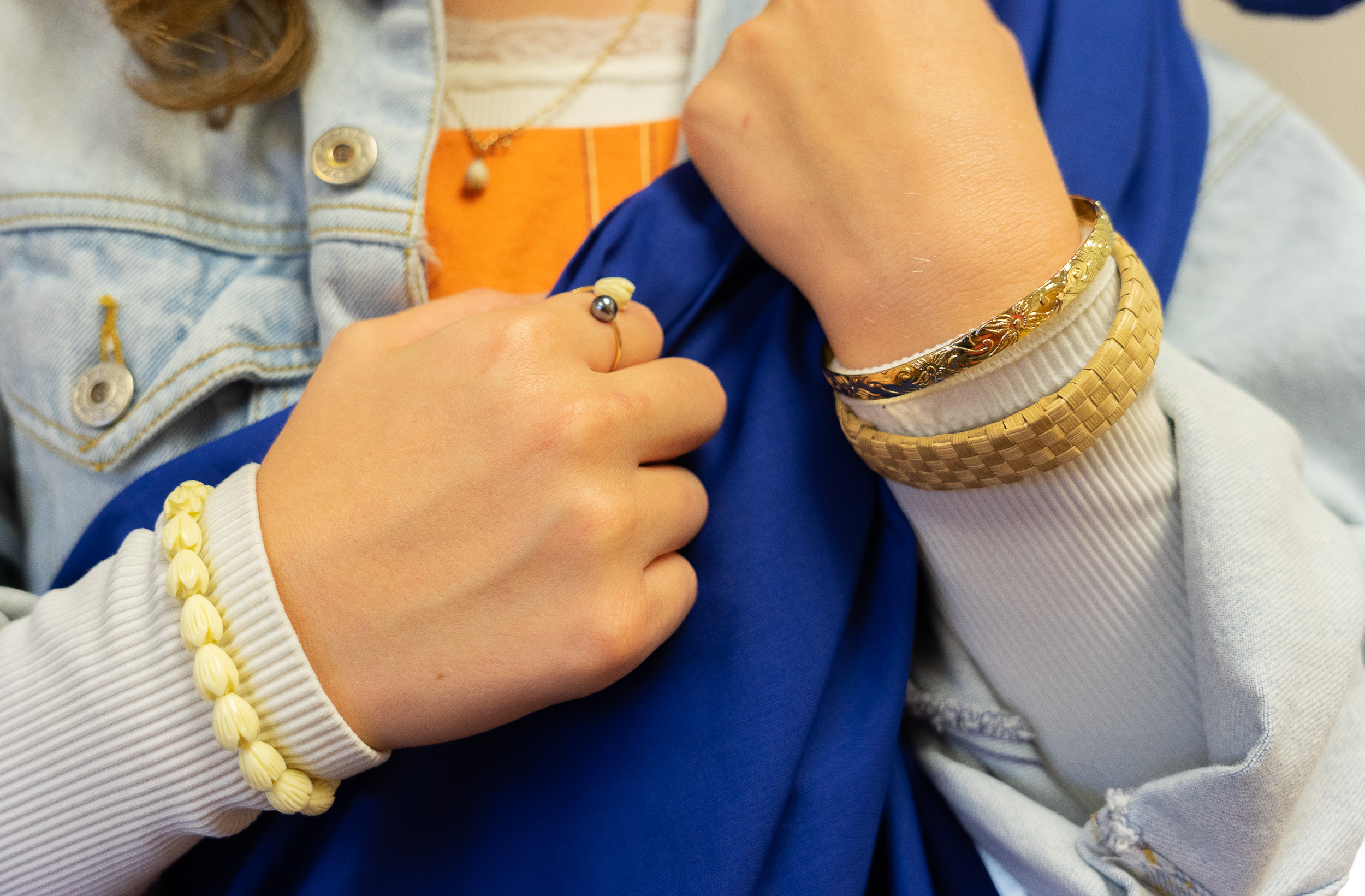 A close-up of a woman’s hands wearing Hawaiian jewelry, including a necklace, a ring and three bracelets.
