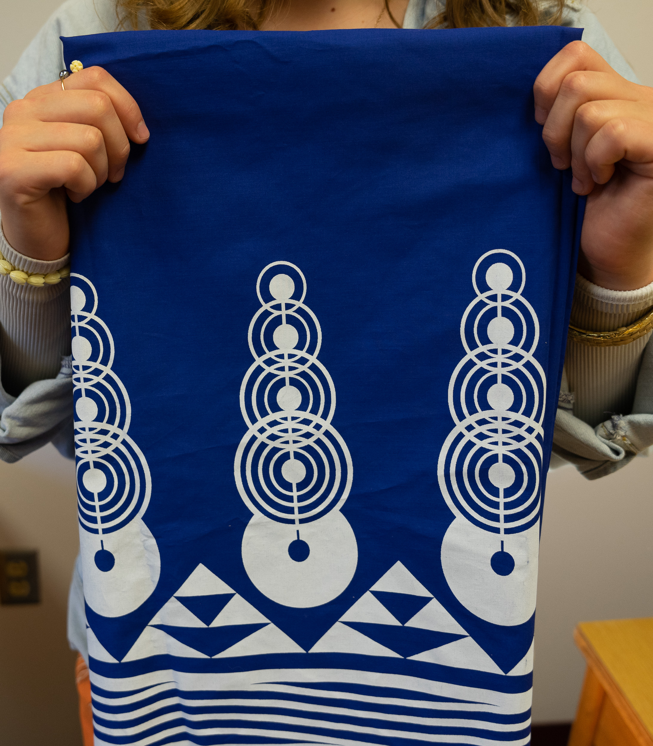 A woman’s hands hold up a blue fabric garment with white patterns on it.