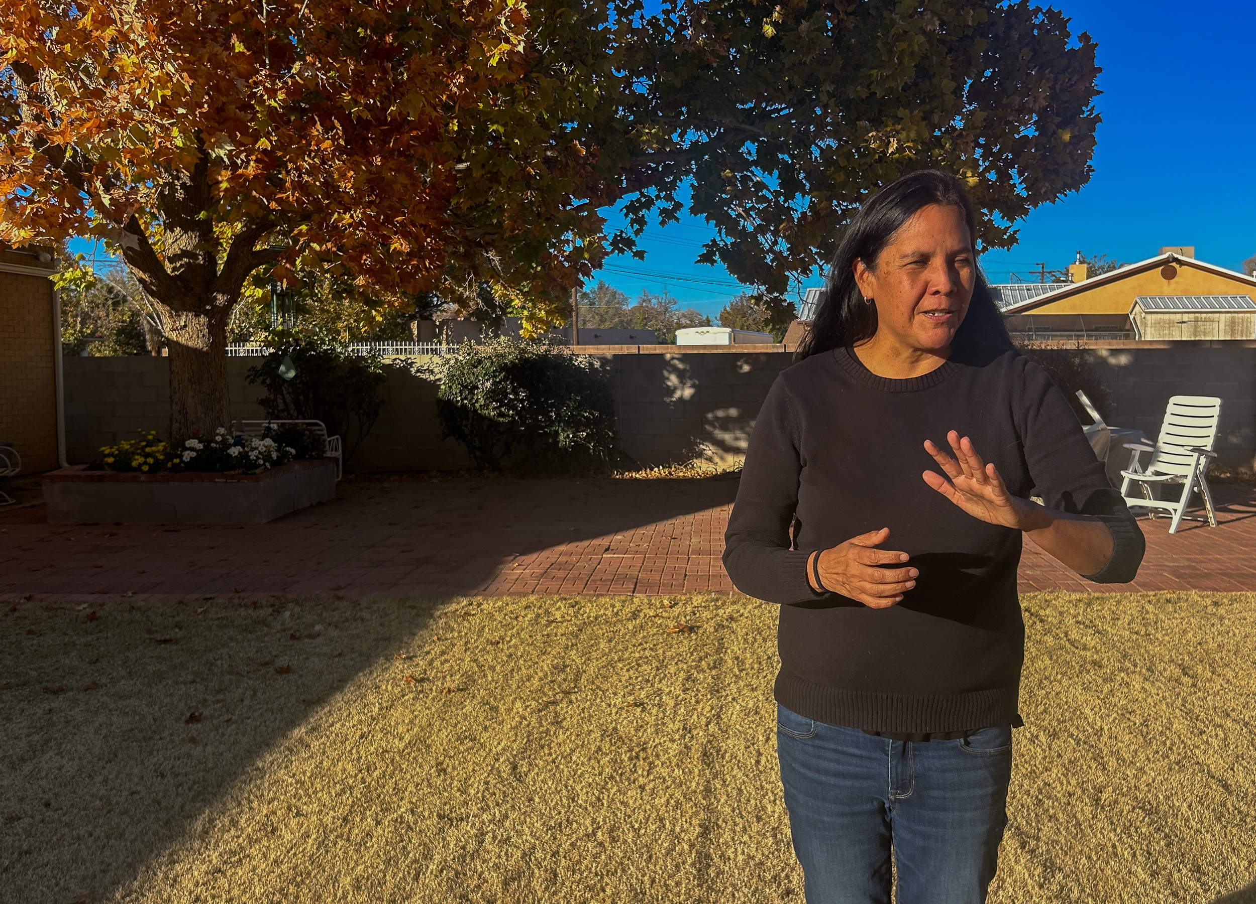 A woman in a sweater and jeans gestures to the space in her grandmother's backyard.